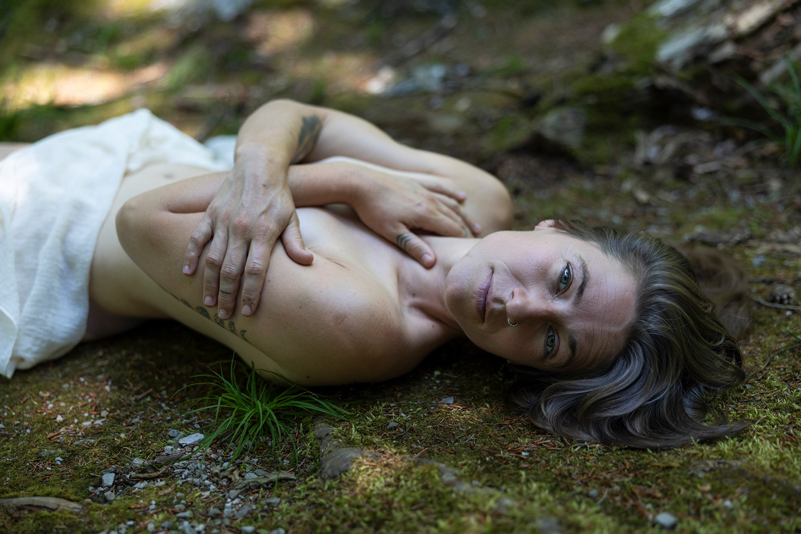 Frau liegt am Waldboden und umarmt sich selbst